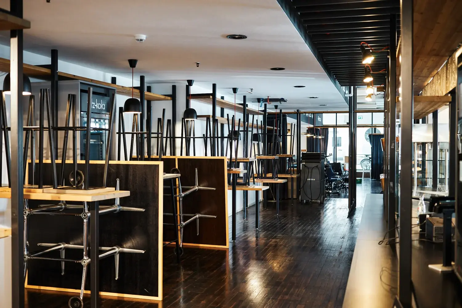 Leeres modernes Restaurant mit umgekehrt gestapelten Tischen und Stühlen, poliertem dunklem Holzboden und schwarzen Pendelleuchten.