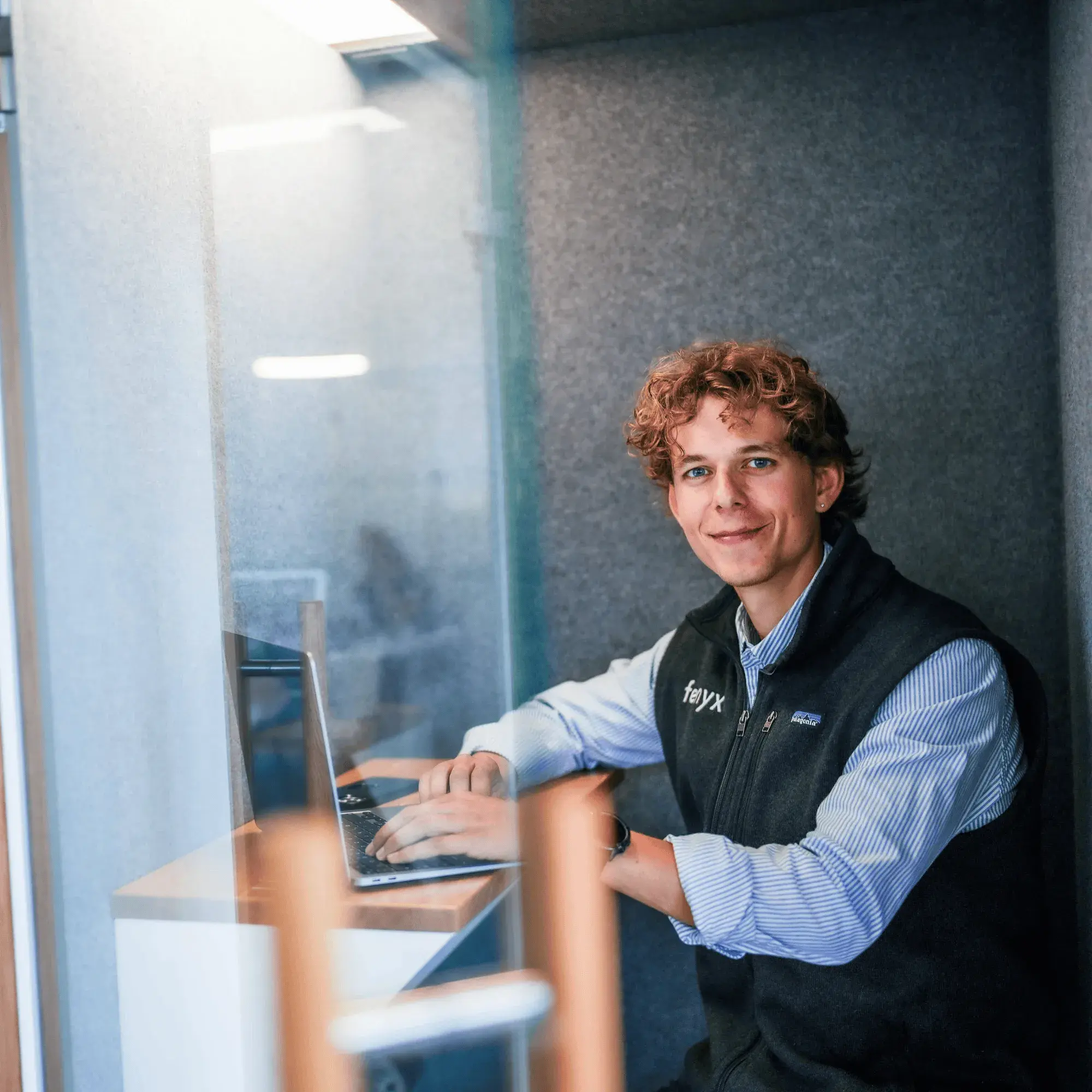 Person arbeitet an einem Schreibtisch in einem modernen Büro mit großen Fenstern.
