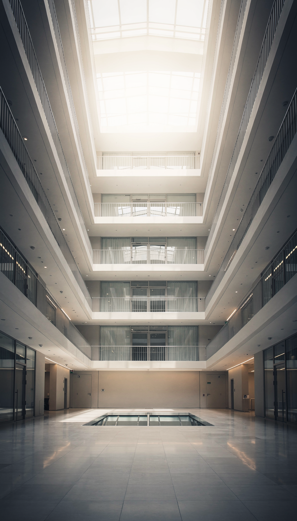 Regard vers le haut dans un atrium de bureau moderne avec façade vitrée et galeries.